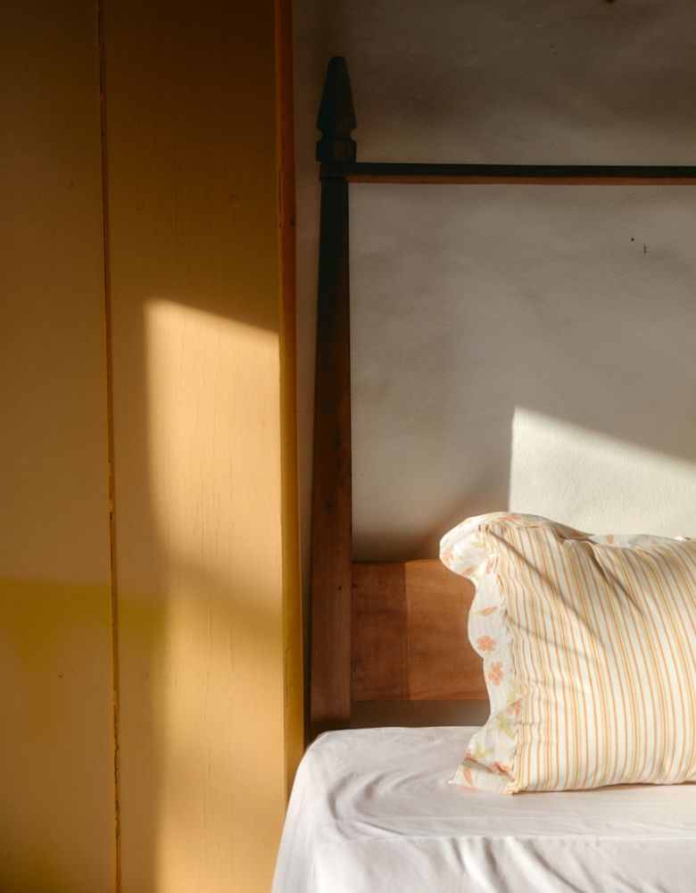 Close up of the side of a bed against a wall with a pillow